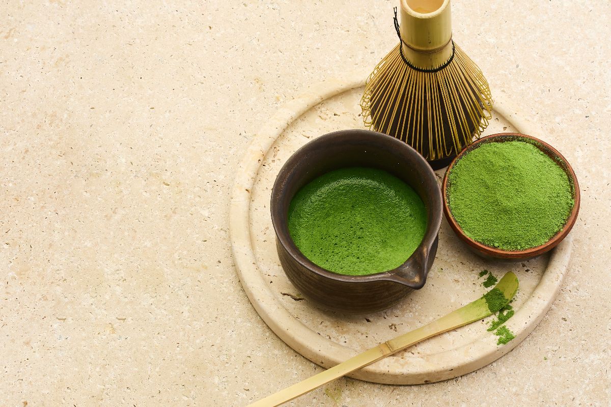 Vista tagliere in legno con ciotola, frustino e tè matcha in polvere