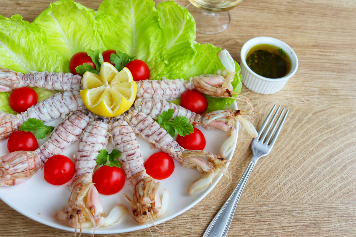 Piatto con canocchie cotte e pulite decorato con insalata, pomodorini e limone