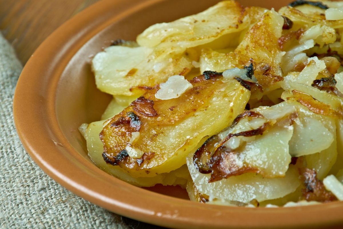 Piatto di terracotta con patate a fette e cipolle