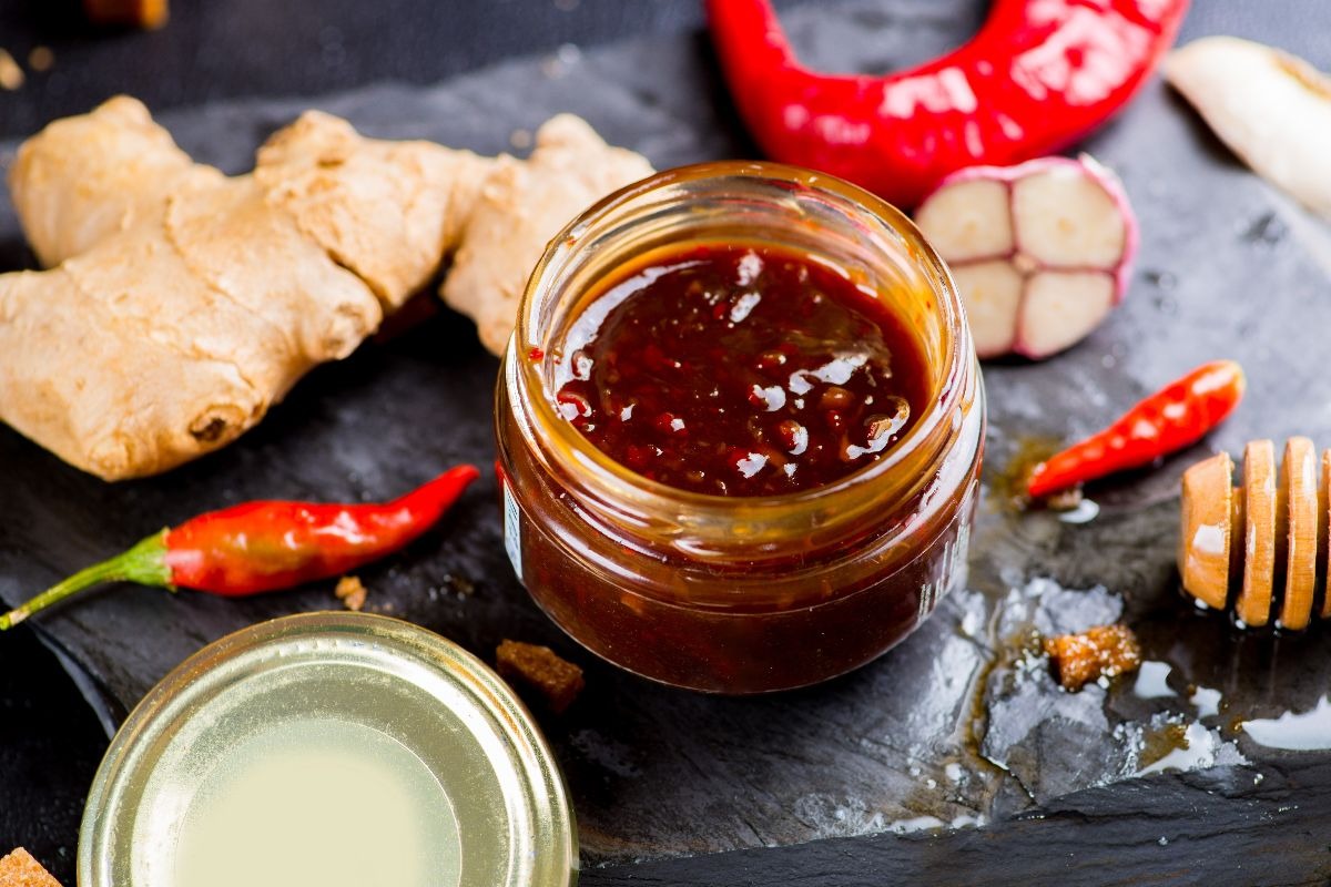 Vasetto di salsa teriyaki con attorno ingredienti per aromatizzarla (zenzero, miele, aglio, peperoncino)