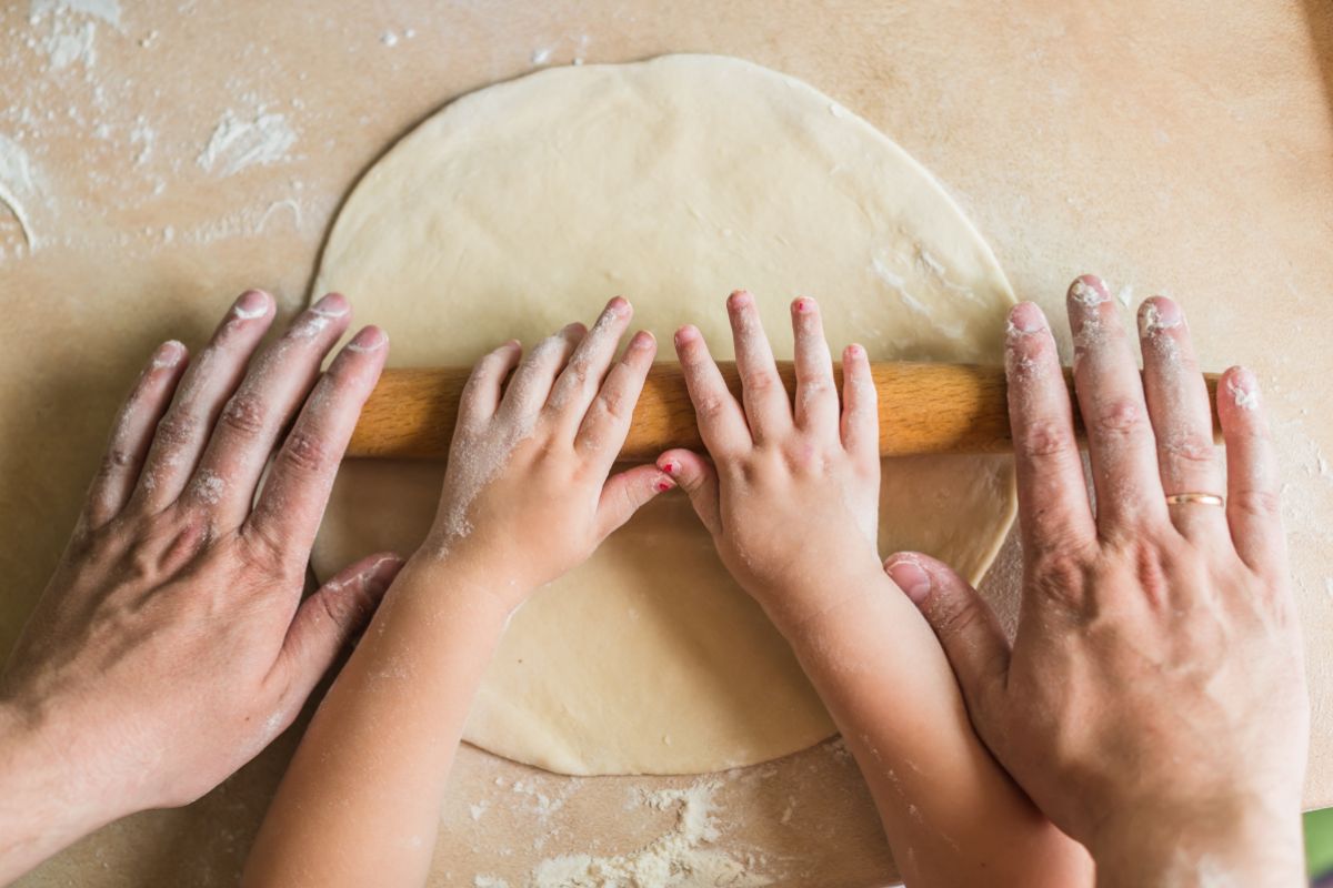 Top view of adult and child hands rolling out dough with a rolling pin