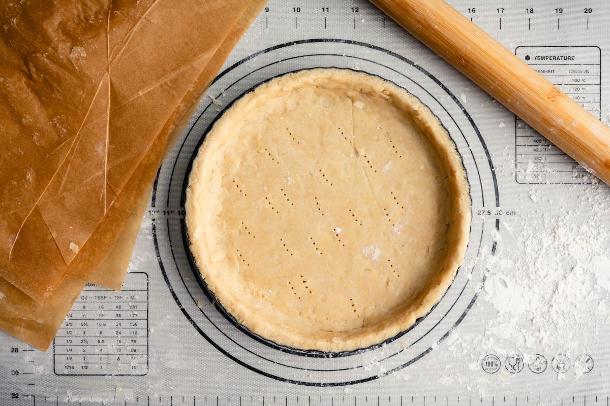 Brisée-type dough spread out on a baking tray seen from above with a rolling pin and baking paper