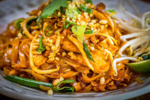 Piatto di pad thai con gamberi, pollo, germogli di soia, lime e arachidi