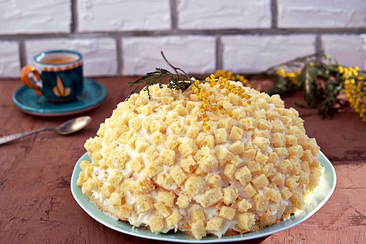 Whole mimosa cake on wooden table with cup of coffee and mimosa flower.