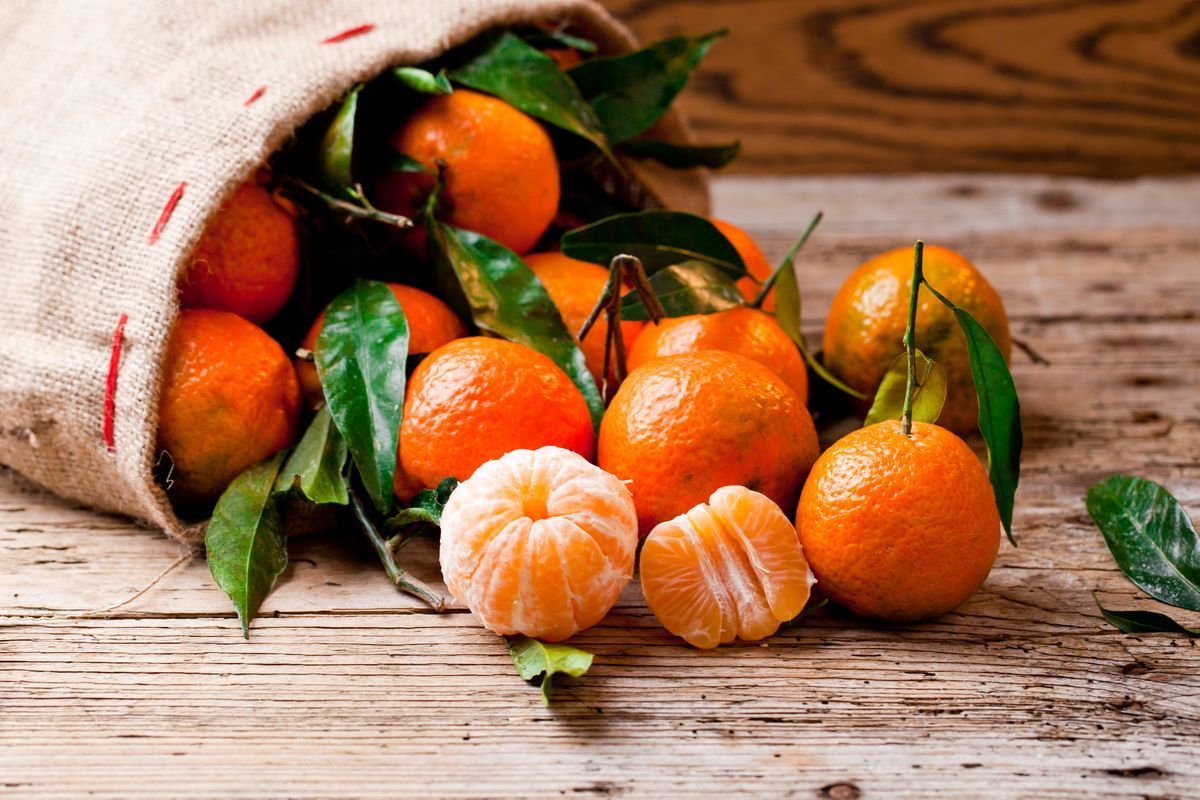 Overturned jute bag from which mandarins emerge, some of which are peeled