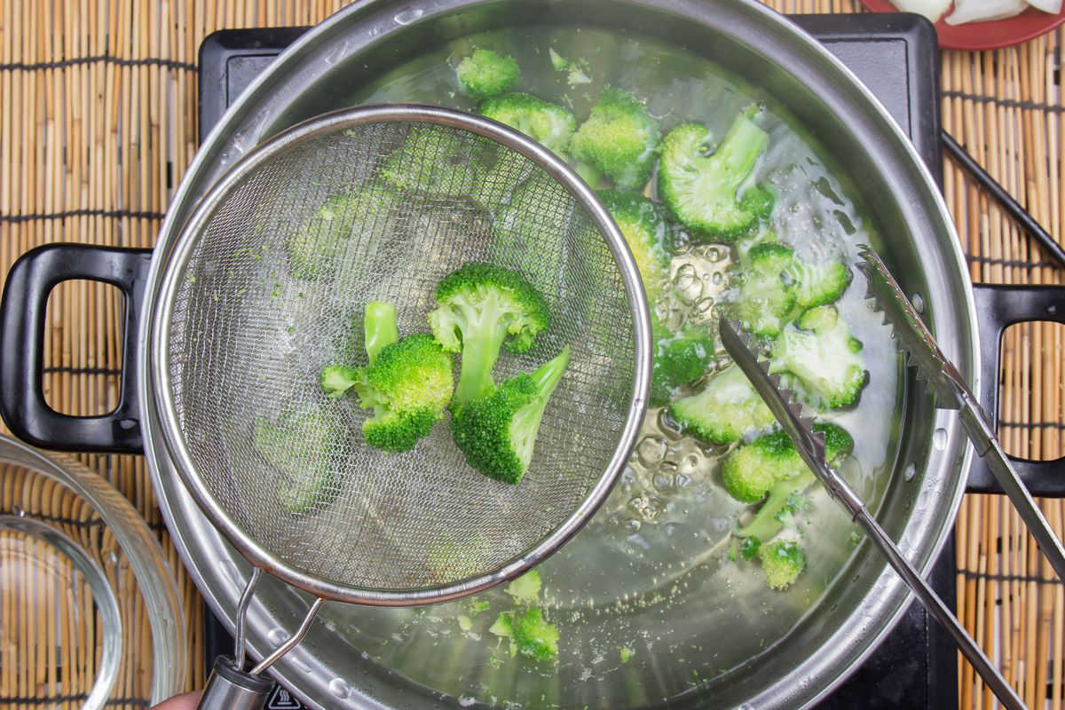 Broccoli in a pot of boiling water with a strainer and tongs