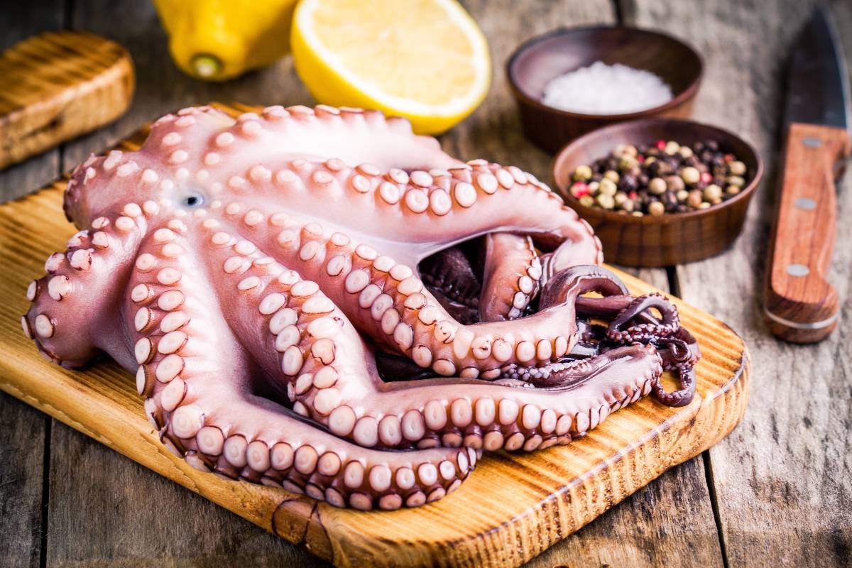 Polpo da cuocere su tagliere in legno con ingredienti di contorno
