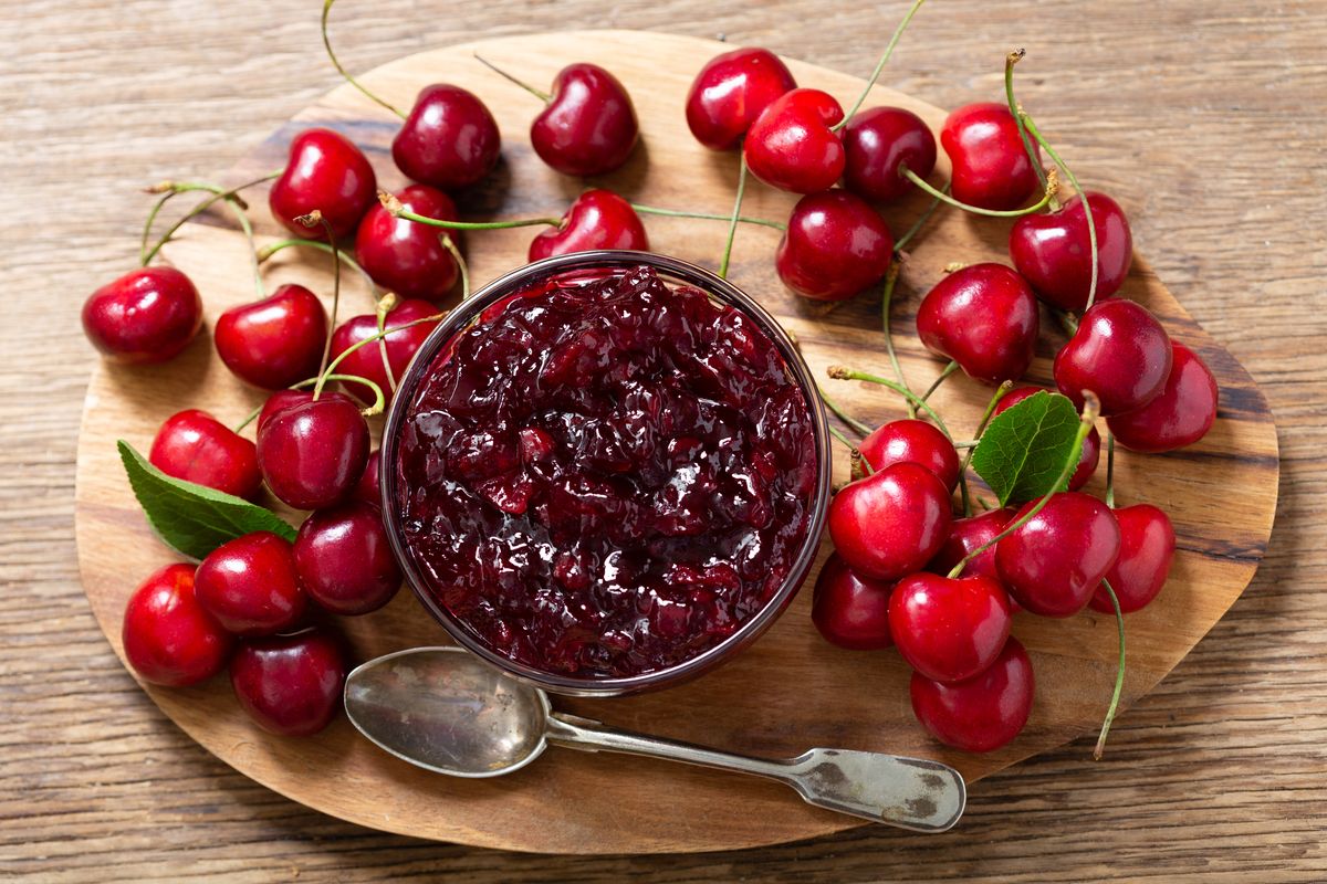 Ciotola di vetro con marmellata di ciliegie e ciliegie fresche attorno