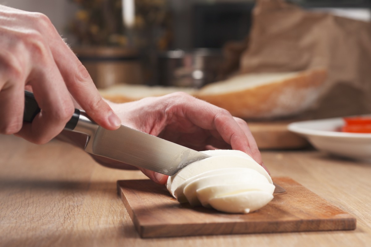 Mani che tagliano a fette mozzarella su tagliere di legno