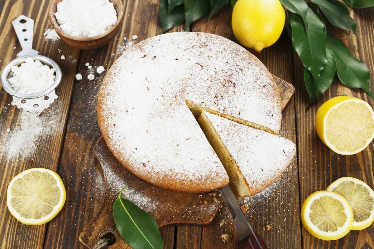 Lemon cake with cut slice and decoration of lemons, lemon leaves and icing sugar