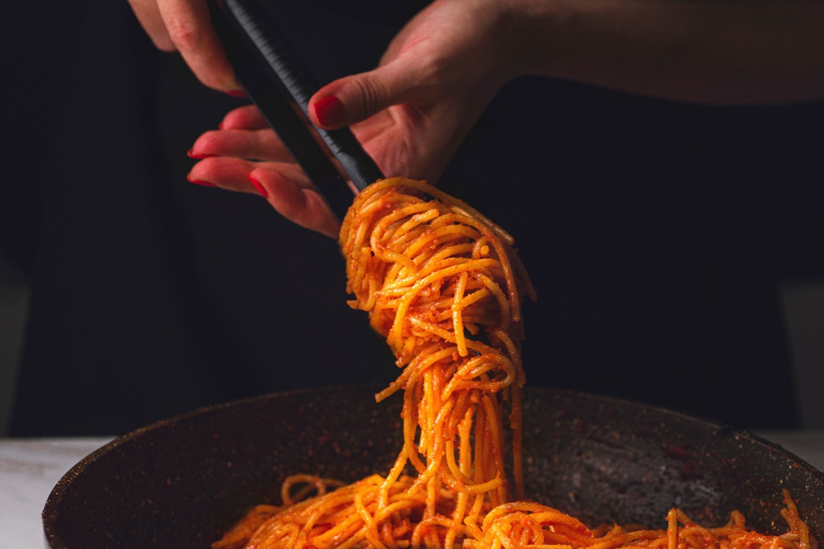 mani che arrotolano spaghetti con il sugo