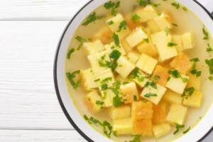 Piatto di brodo visto dall'alto con cubetti di pasta e prezzemolo