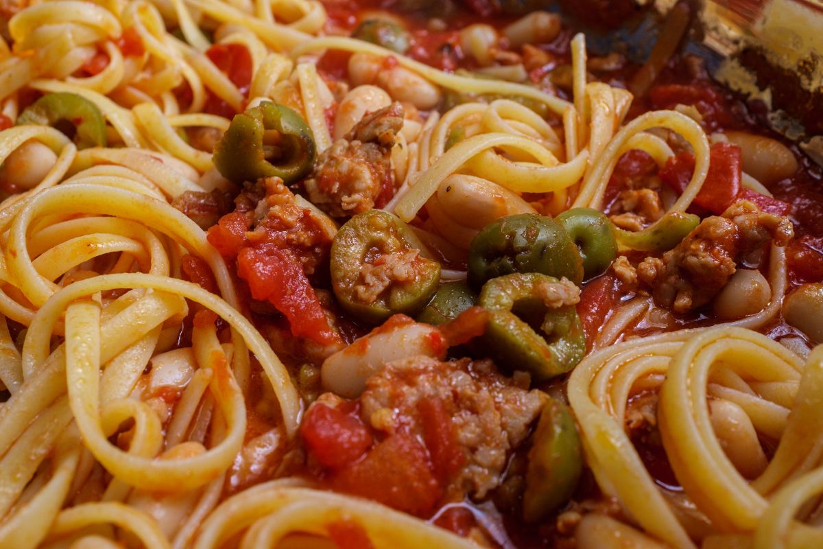 Pasta linguine con sugo di pomodoro a pezzi, salsiccia e olive a rondelle