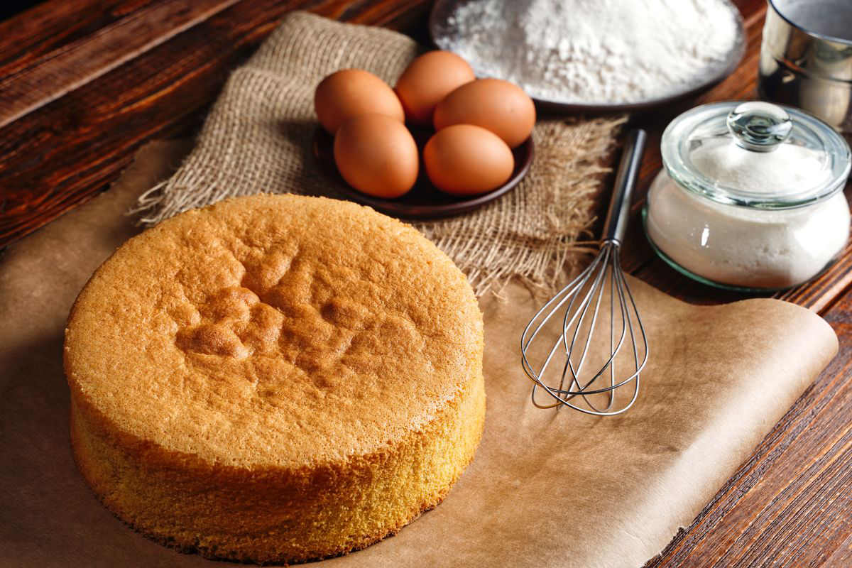 Sponge cake on the table with eggs, flour, sugar and kitchen whisk