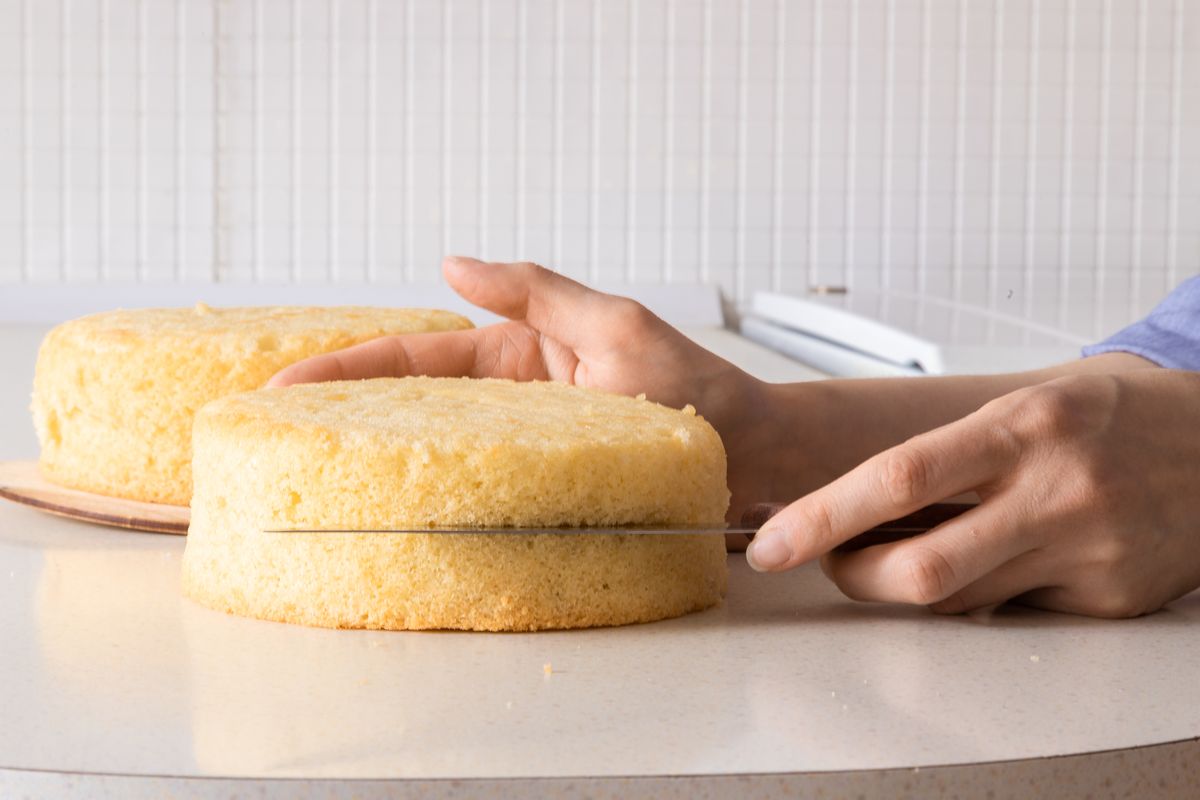 Woman cutting sponge cake in half with knife.