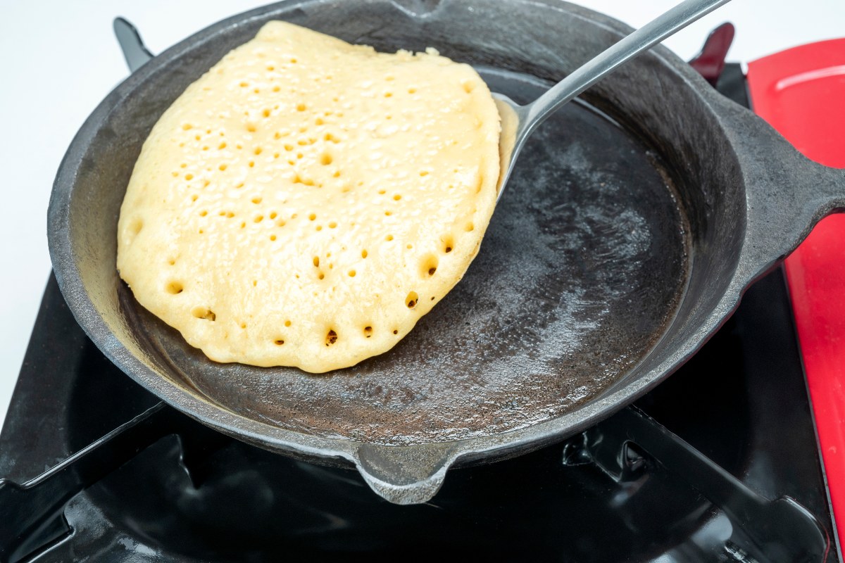 Pancake che sta per essere girato per cuocere dall'altro lato in padella con paletta da cucina.