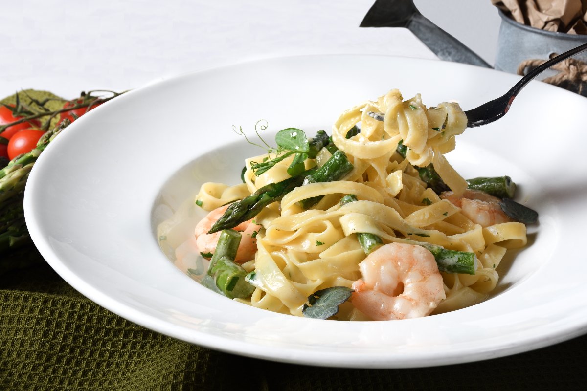 Piatto di pasta tagliatelle con asparagi e gamberetti e forchetta