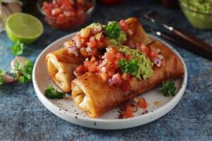 Piatto tea-mex noto come chimichanga, tortilla ripiena servita con guacamole e pomodori a dadini