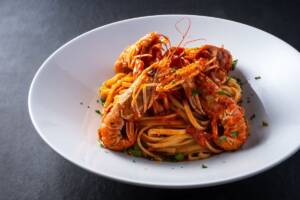 Piatto di pasta tipo spaghetti con sugo di pomodoro e scampi