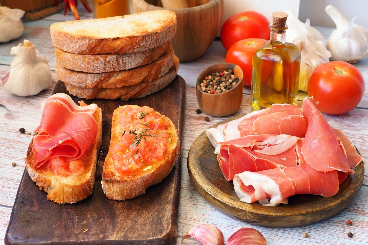 Bruschette di pane con purea di pomodoro e prosciutto crudo su tagliere di legno