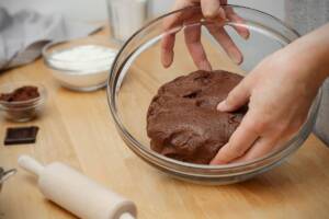 Panetto di pasta frolla al cacao in ciotola di vetro con mani di donna