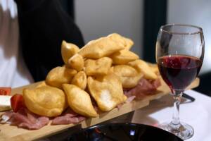 Tagliere con impasto fritto e salumi vicino a calice di vino
