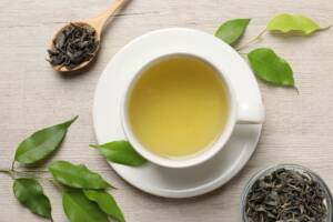 Una tazza di té verde con e cucchiaio e foglie sul tavolo