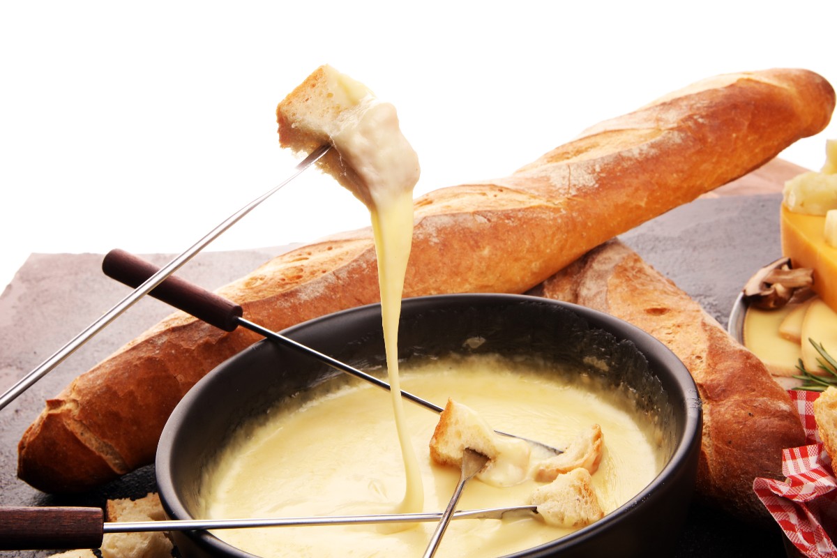 Pezzo di pane intinto nel formaggio fuso, con una baguette sullo sfondo.