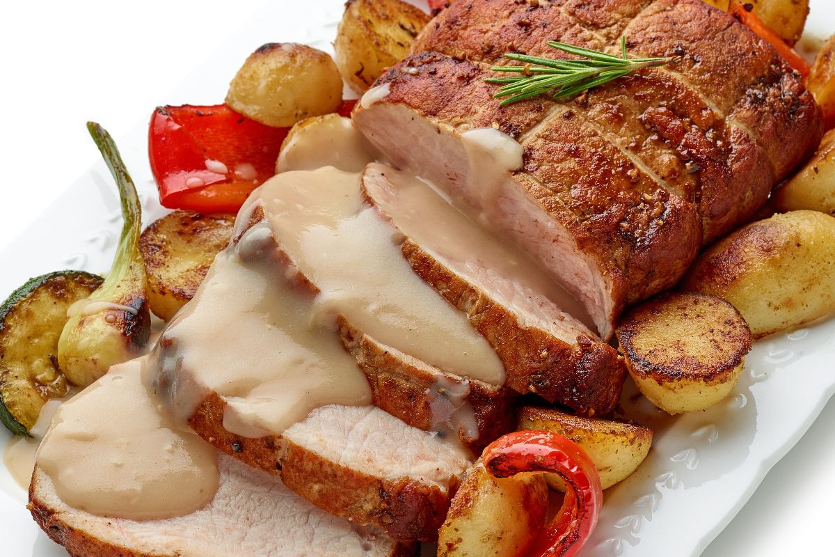 Piatto con arrosto di maiale a fette, sugo e patate al forno