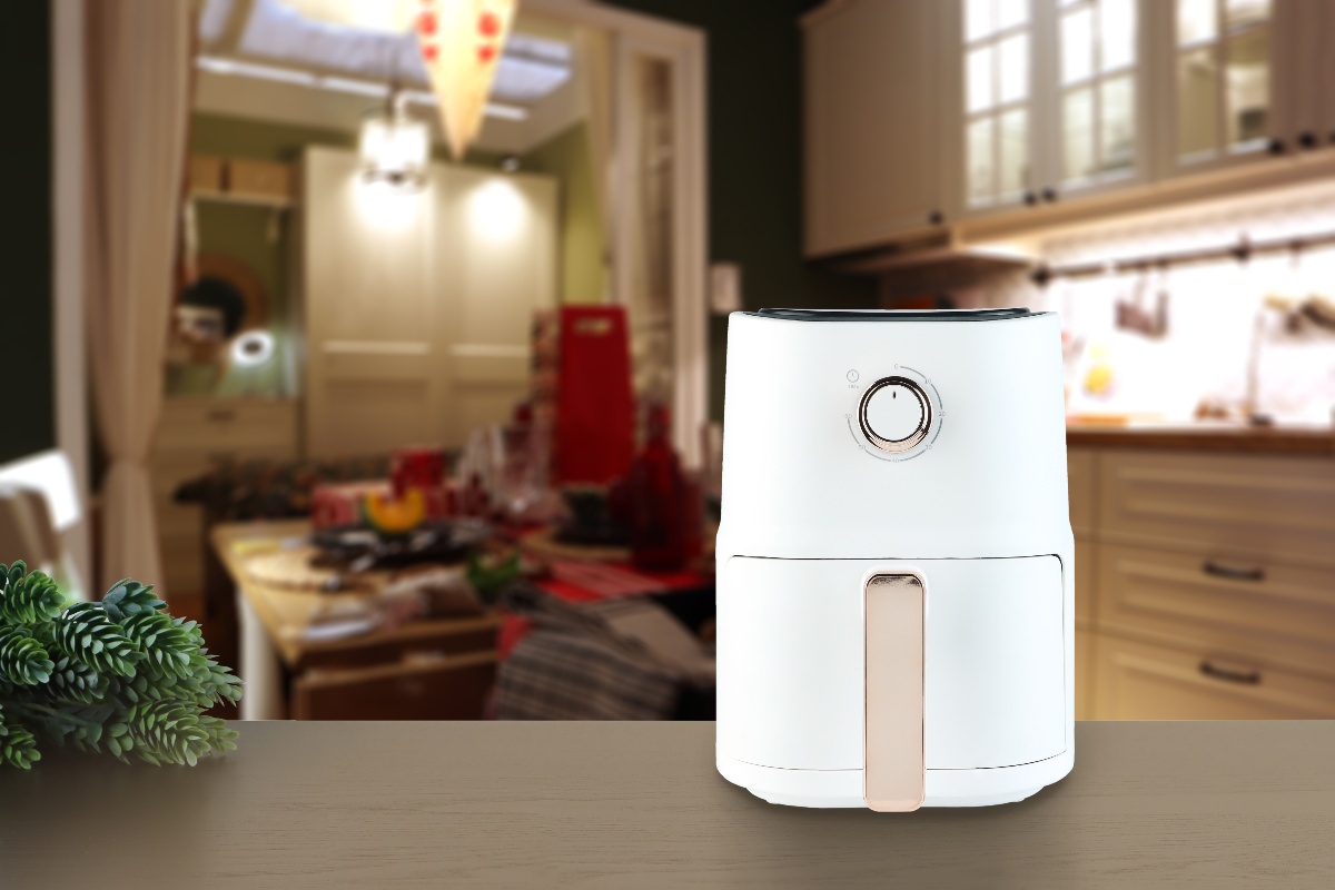 Friggitrice ad aria posata su tavolo da cucina con ramo di pino vicino e cucina sullo sfondo