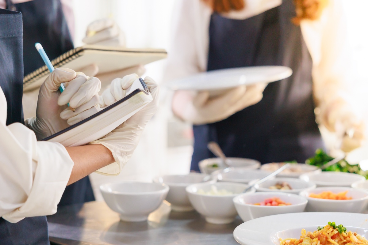 Scuola di cucina: allievi che scrivono appunti con gli ingredienti pronti sul tavolo.