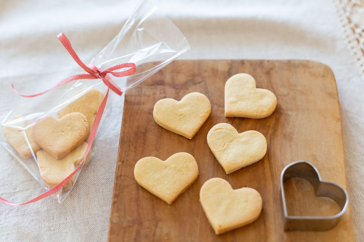 Biscotti di pasta frolla a forma di cuore su tagliere in legno e in sacchetto di plastica con nastrino