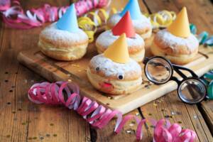 Tagliere di legno con bomboloni decorati con cappellino colorato per Carnevale e stelle filanti vicino