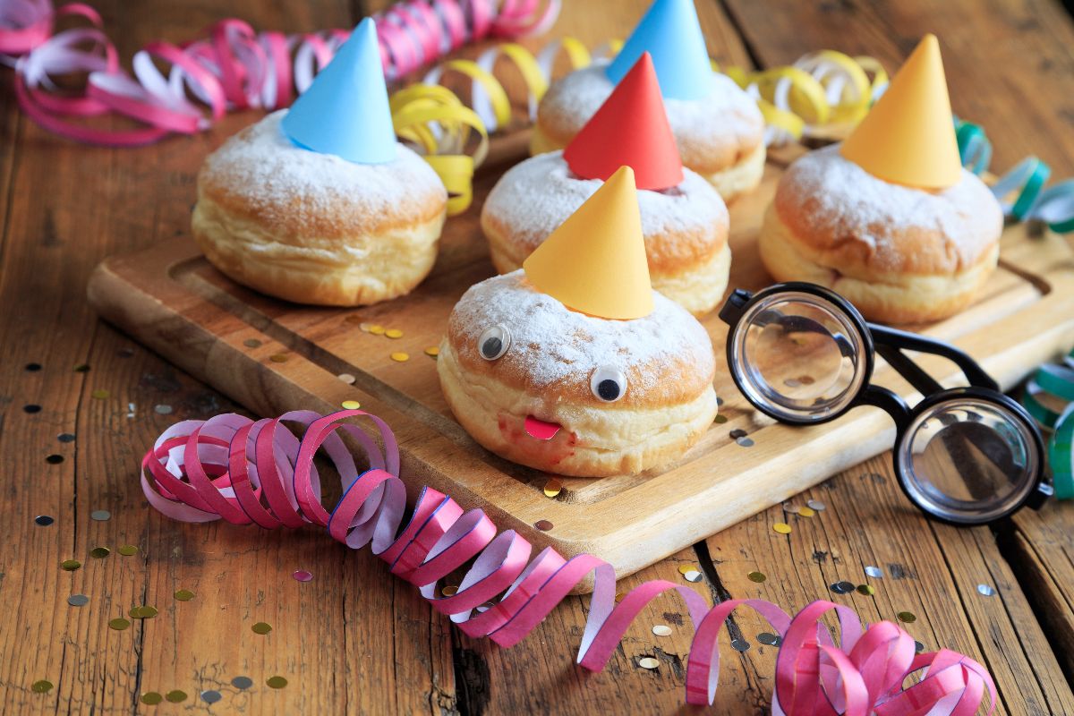 Tagliere di legno con bomboloni decorati con cappellino colorato per Carnevale e stelle filanti vicino