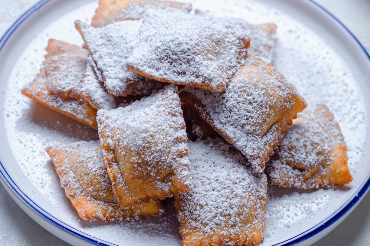 Ravioli dolci fritti cosparsi di zucchero a velo su piatto bianco