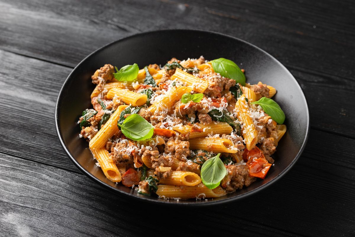 Piatto di pasta condita con ragù e spinaci e completata con formaggio grattugiato