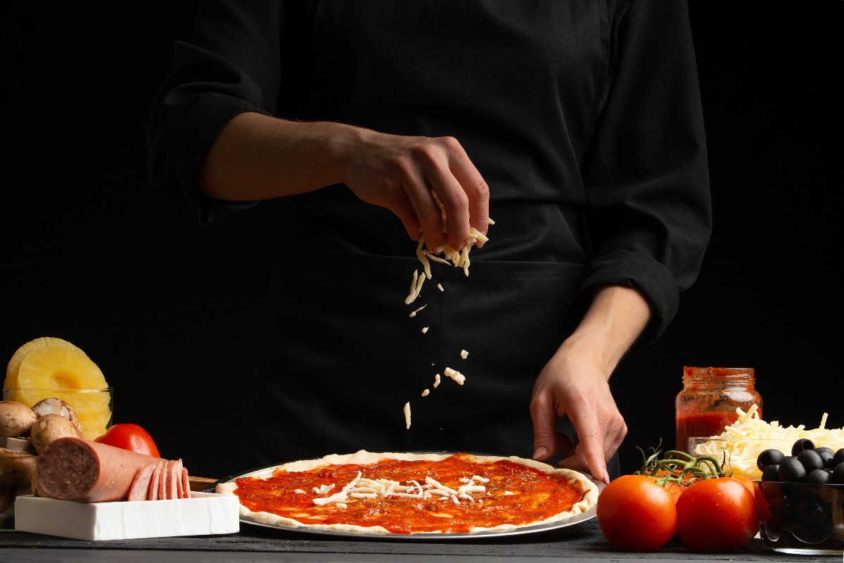 Un cuoco intento a distribuire la mozzarella fresca sopra una pizza stesa.