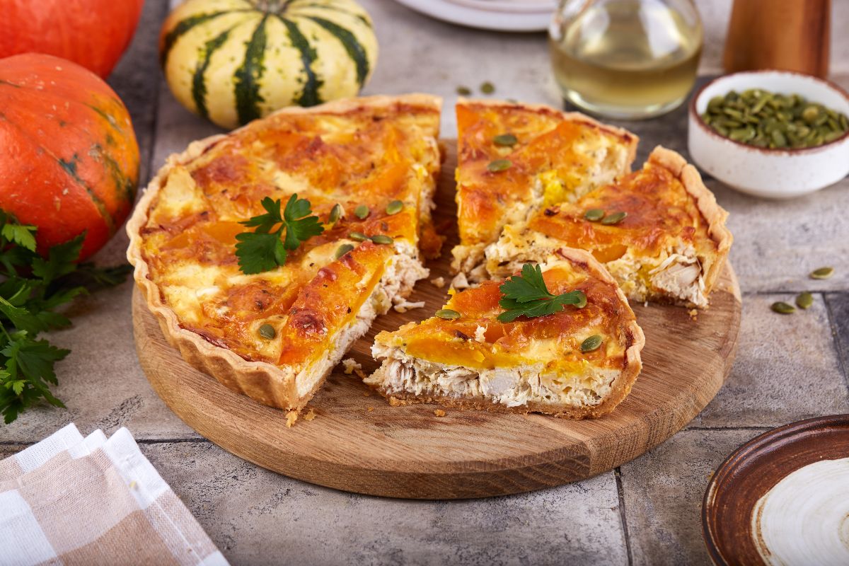 Una torta salata con pollo e zucca servita su un tagliere rotondo di legno.