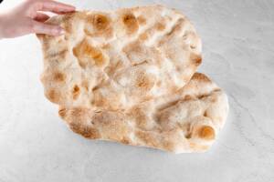 Mano femminile che mostra una base precotta per pinsa romana