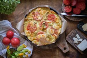 Vista dall'alto impasto pizza a base di zucchine farcito con mozzarella, pomodoro a fette e fiori di zucca
