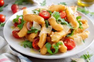 Pasta fritta servita con rucola, pomodorini e grana